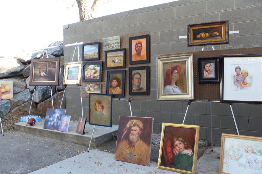 A wide outdoor display of framed portraits, landscapes, and still lifes on easels and pegboards